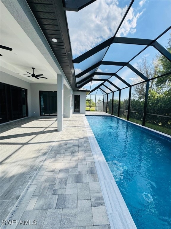 outdoor pool featuring a ceiling fan, glass enclosure, and a patio