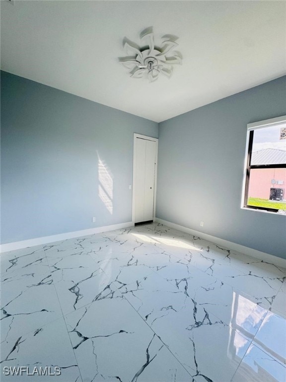 empty room with ceiling fan, marble finish floor, and baseboards