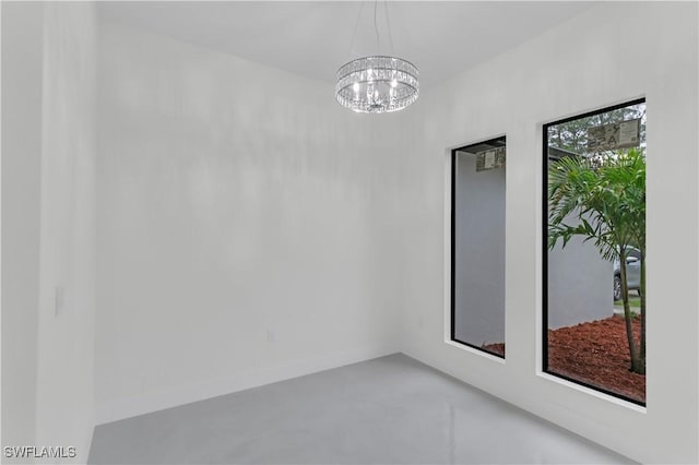 spare room featuring finished concrete flooring, baseboards, and a chandelier