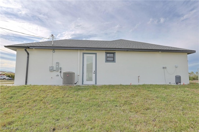 back of property with a shingled roof, central AC, a yard, and stucco siding