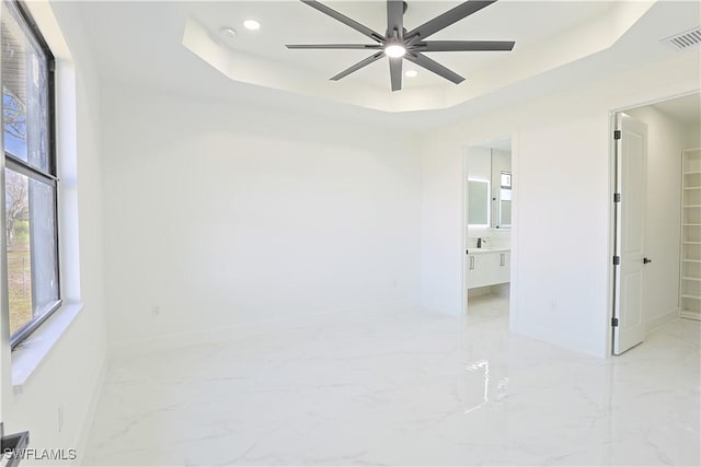 spare room with marble finish floor, a raised ceiling, visible vents, and baseboards