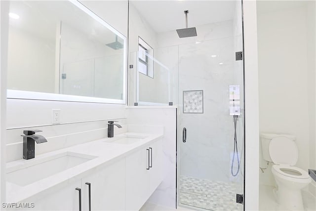 full bathroom featuring toilet, double vanity, a sink, and a marble finish shower