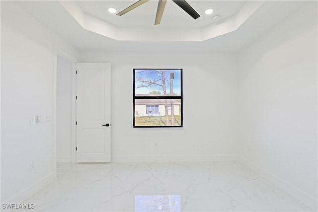 empty room with a tray ceiling, marble finish floor, recessed lighting, ceiling fan, and baseboards