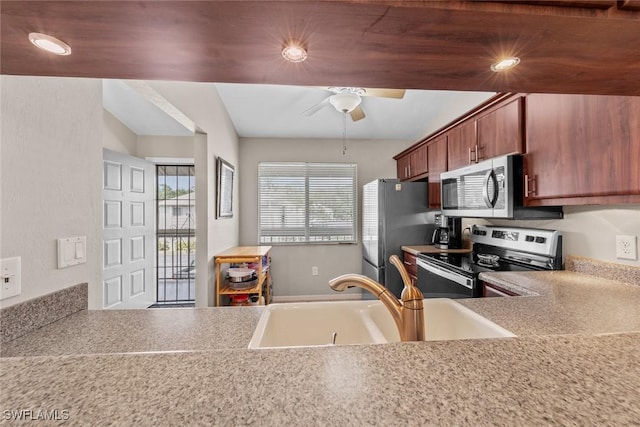 kitchen with stainless steel appliances, a sink, a ceiling fan, light countertops, and brown cabinetry
