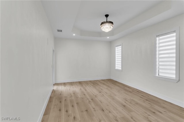 spare room with baseboards, visible vents, a raised ceiling, light wood-style flooring, and an inviting chandelier