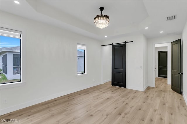 unfurnished bedroom featuring recessed lighting, a raised ceiling, visible vents, a barn door, and baseboards