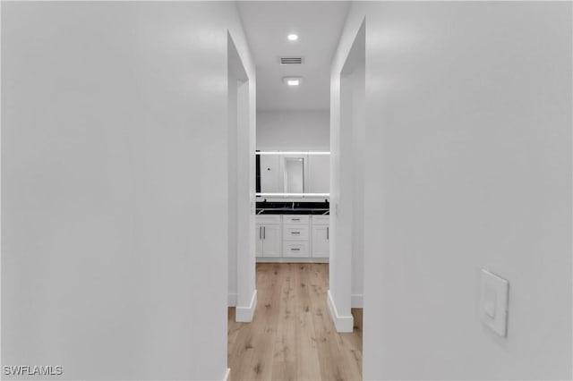 hallway featuring light wood-style floors, visible vents, and baseboards