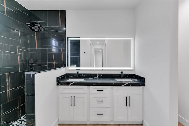 full bathroom with double vanity, walk in shower, and baseboards