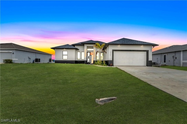 prairie-style home with a garage, central AC, concrete driveway, a yard, and stucco siding