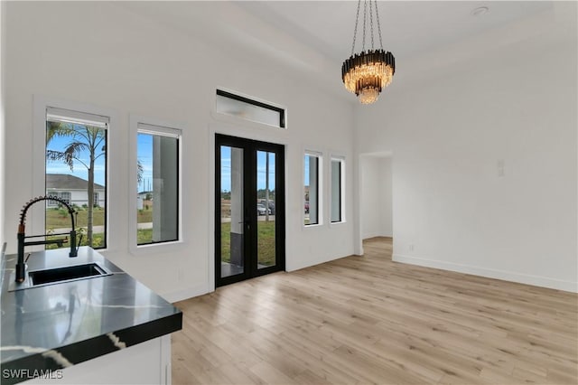 entrance foyer with french doors, a notable chandelier, light wood finished floors, a towering ceiling, and baseboards