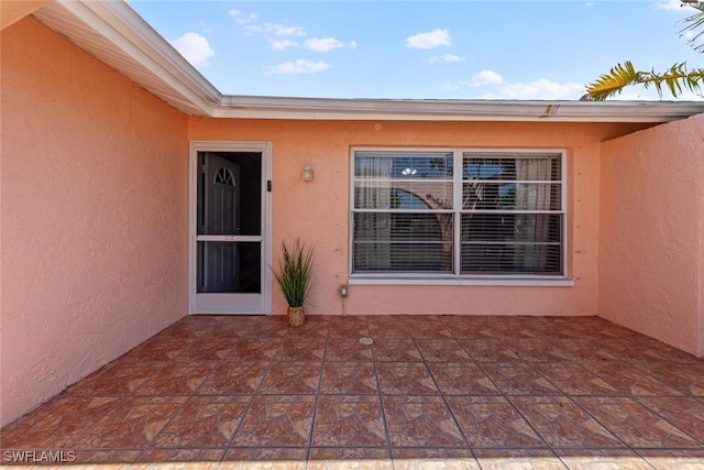 view of exterior entry with a patio area and stucco siding