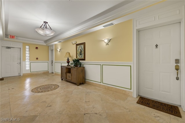 entrance foyer featuring a tray ceiling, a wainscoted wall, visible vents, a decorative wall, and ornate columns