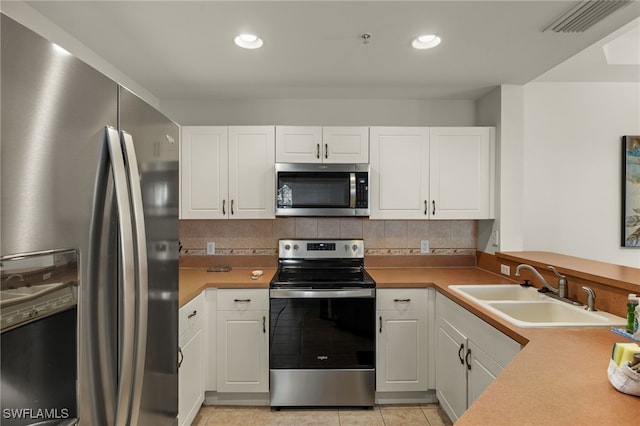 kitchen featuring appliances with stainless steel finishes, light tile patterned flooring, a sink, and white cabinetry