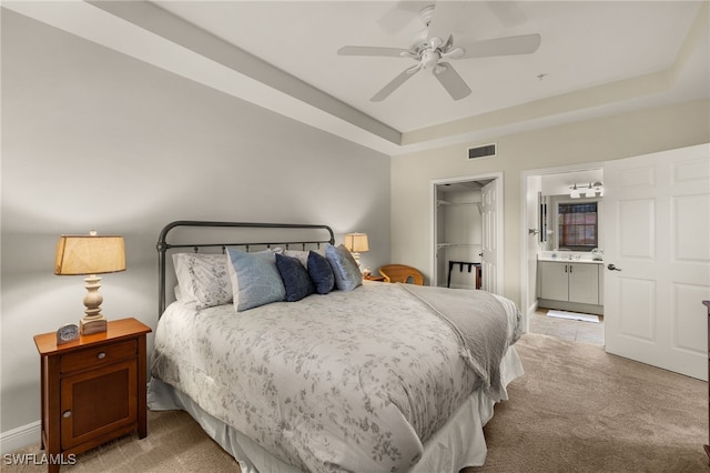 bedroom with visible vents, a raised ceiling, connected bathroom, carpet, and a walk in closet