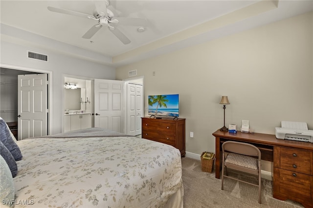 carpeted bedroom featuring a tray ceiling, visible vents, ensuite bath, and baseboards