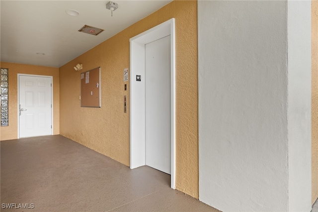 hall featuring concrete floors, elevator, and a textured wall