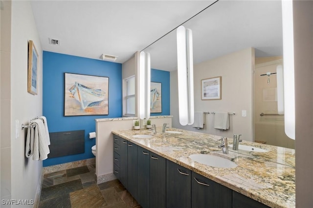 bathroom featuring stone finish flooring, visible vents, toilet, and double vanity