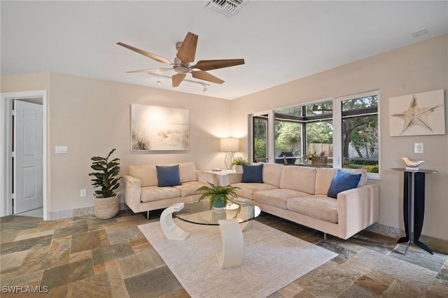 living room featuring stone finish flooring, visible vents, ceiling fan, and baseboards