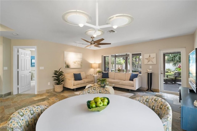 living area featuring stone finish flooring, a ceiling fan, visible vents, and baseboards