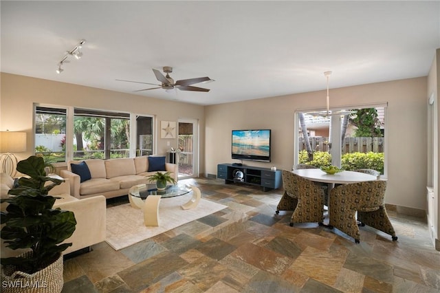 living area with a ceiling fan, stone finish flooring, and baseboards