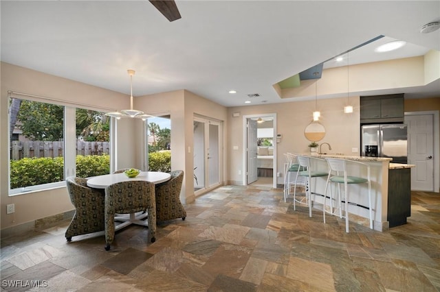 kitchen featuring pendant lighting, stainless steel refrigerator with ice dispenser, stone finish flooring, a kitchen breakfast bar, and baseboards