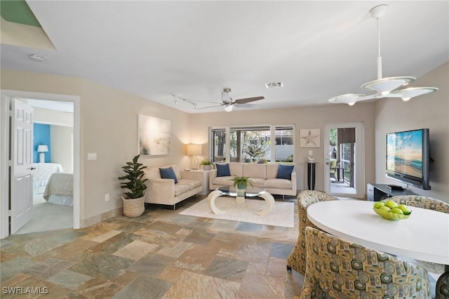 living room with a ceiling fan, visible vents, baseboards, stone finish floor, and rail lighting