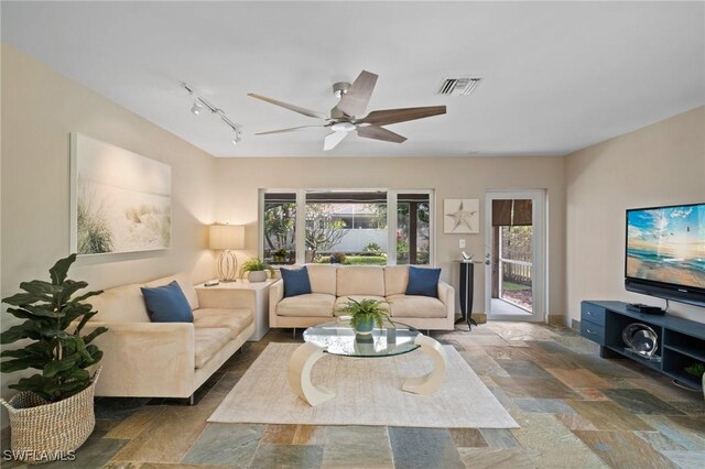 living area featuring visible vents, baseboards, a ceiling fan, stone finish flooring, and track lighting