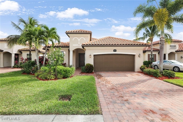 mediterranean / spanish-style house featuring decorative driveway, a tile roof, stucco siding, an attached garage, and a front lawn