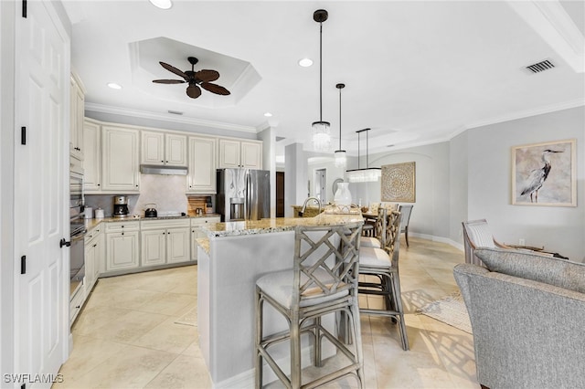 kitchen with light stone counters, under cabinet range hood, ornamental molding, stainless steel fridge with ice dispenser, and cooktop