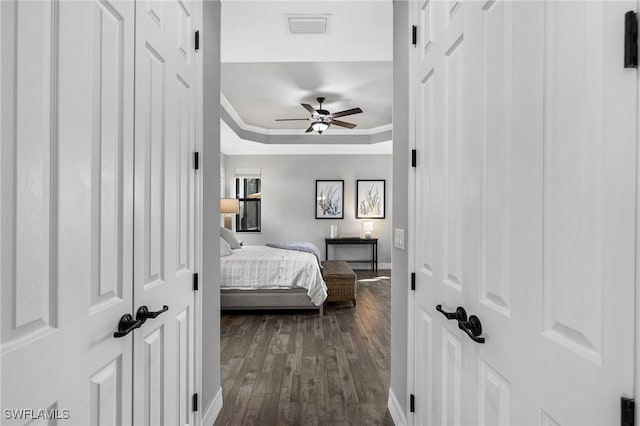 bedroom featuring ceiling fan, visible vents, a tray ceiling, dark wood finished floors, and crown molding