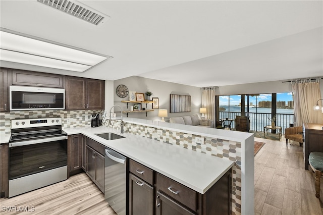 kitchen featuring a peninsula, a sink, visible vents, open floor plan, and appliances with stainless steel finishes