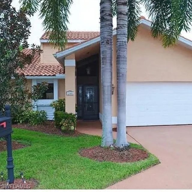 doorway to property with a garage, concrete driveway, a yard, and a tile roof