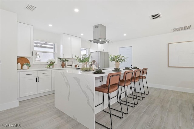 kitchen featuring an island with sink, island exhaust hood, visible vents, and freestanding refrigerator