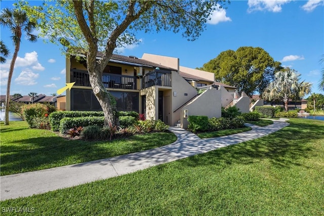 view of front of house with a front yard, a balcony, and stucco siding