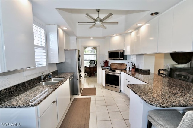 kitchen featuring appliances with stainless steel finishes, white cabinets, a sink, and a peninsula