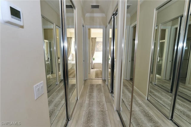 corridor featuring light wood-style flooring, visible vents, and crown molding