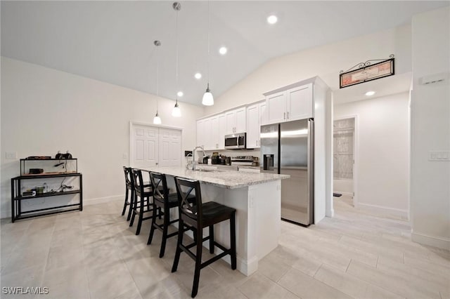 kitchen with light stone counters, stainless steel appliances, white cabinets, a kitchen island with sink, and a kitchen breakfast bar