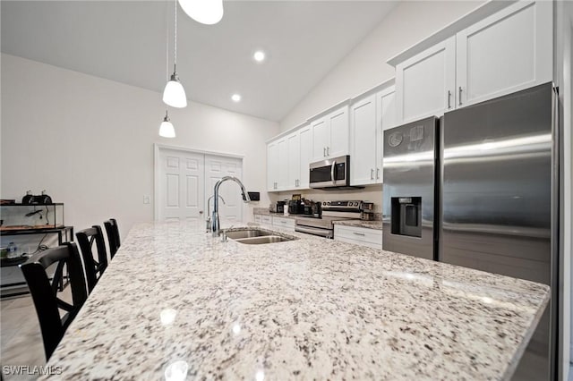 kitchen with light stone counters, a center island with sink, stainless steel appliances, white cabinets, and a sink