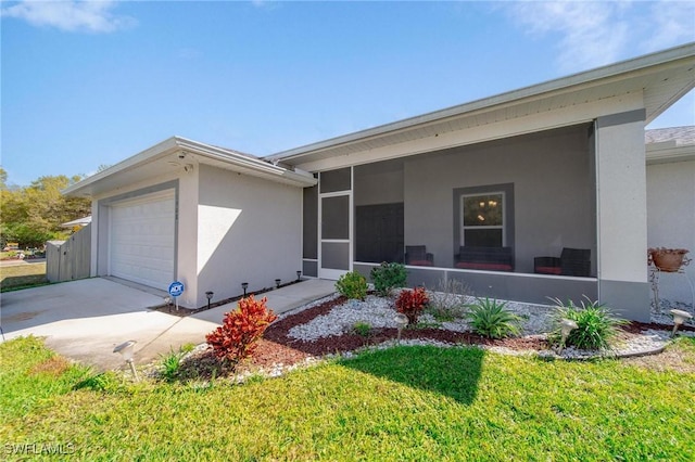 ranch-style home featuring driveway, a sunroom, an attached garage, a front lawn, and stucco siding