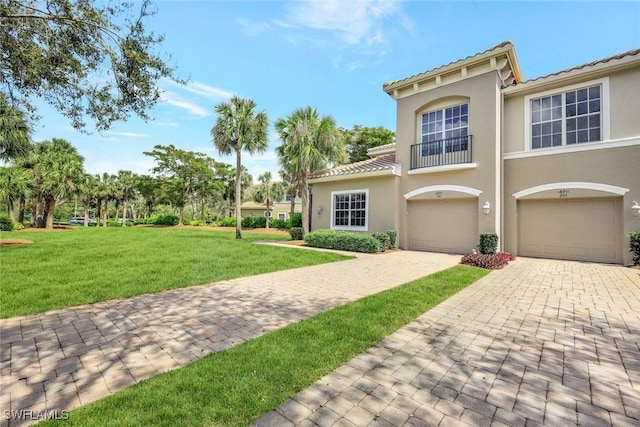 view of front facade featuring a tiled roof, a front yard, stucco siding, decorative driveway, and an attached garage