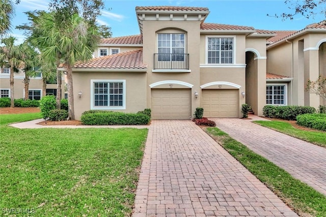 mediterranean / spanish-style home featuring a tiled roof, an attached garage, decorative driveway, a front lawn, and stucco siding