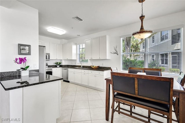 kitchen with a peninsula, a sink, white cabinets, appliances with stainless steel finishes, and dark stone counters