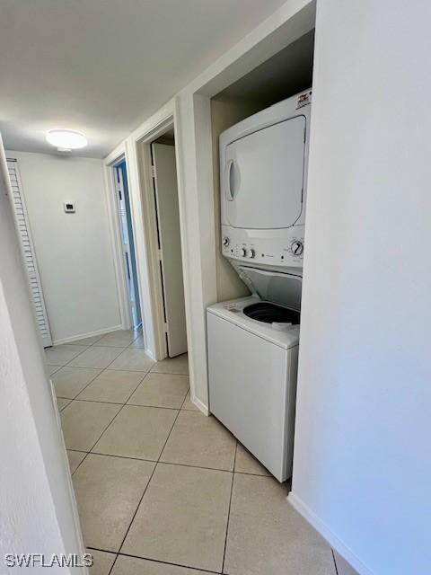 laundry room with stacked washing maching and dryer, baseboards, laundry area, and light tile patterned flooring