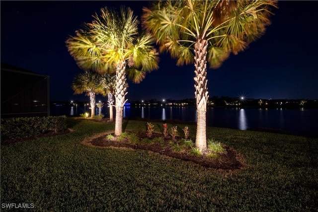 yard at night featuring a water view