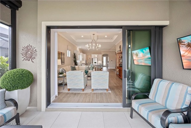 doorway with light tile patterned floors, a raised ceiling, a textured wall, ornamental molding, and a chandelier