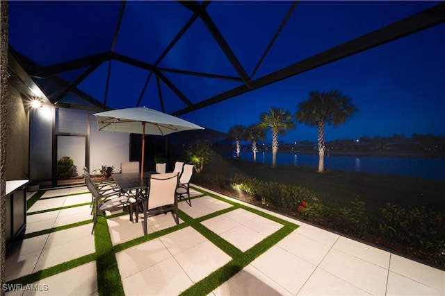 patio at night featuring glass enclosure and a water view