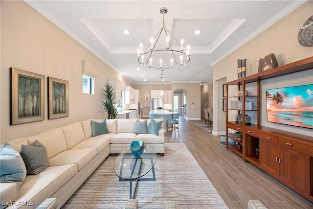 living area featuring light wood finished floors, baseboards, arched walkways, ornamental molding, and an inviting chandelier