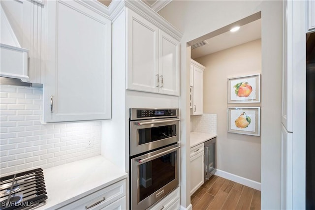 kitchen featuring double oven, wood finished floors, light countertops, and white cabinetry