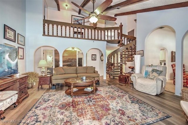 living room featuring light wood finished floors, stairs, arched walkways, and beamed ceiling