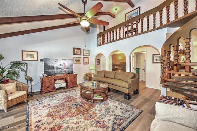 living room featuring arched walkways, ceiling fan, beamed ceiling, and wood finished floors